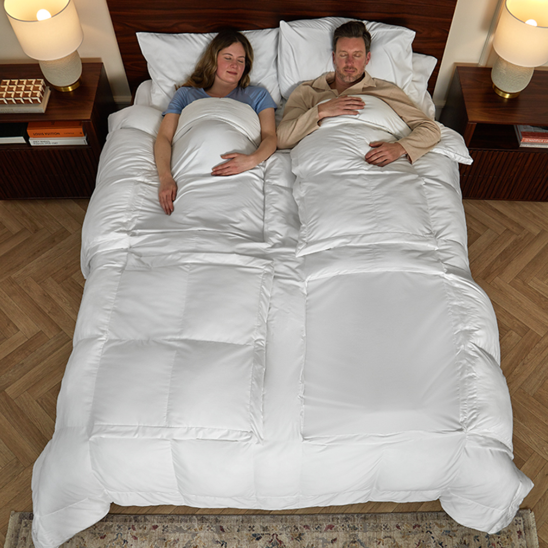 Two people lying in bed under a Sleeping Dove Cooling Comforter with a few windows open showing how it cools you off naturally