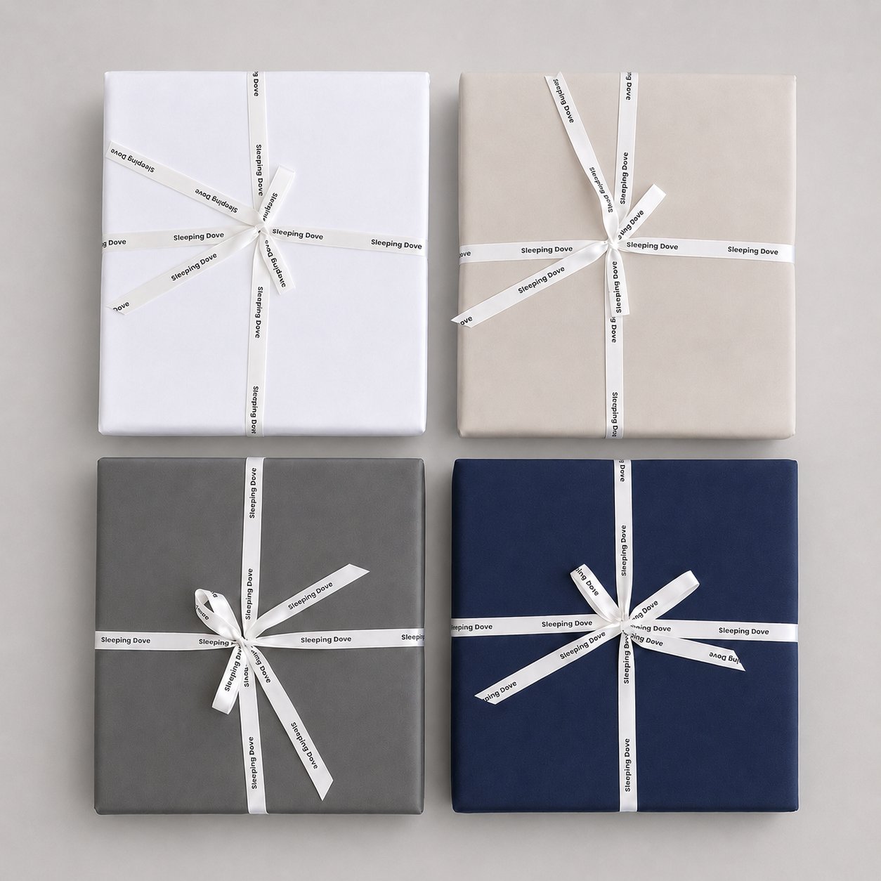 Four wrapped gift boxes from the sleeping dove cooling comforer arranged in a 2x2 grid on a light gray background. The boxes are white, stone, slate, and navy.