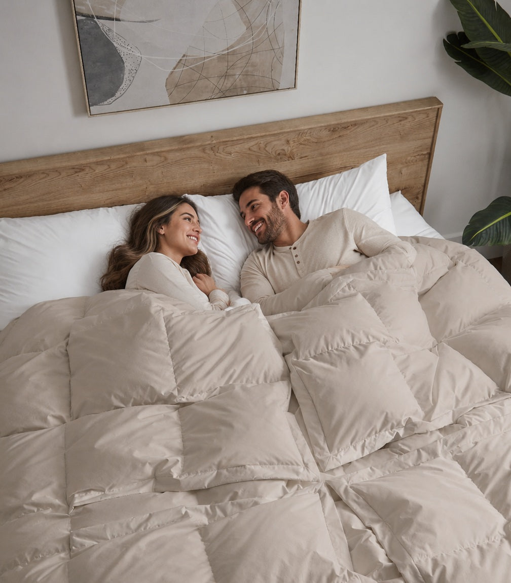A couple smiling at each other in bed under a Sleeping Dove comforter.
