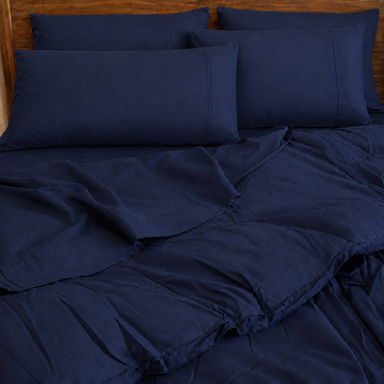 A neatly made bed with navy sleeping dove bedding, including two pillowcases, a duvet cover, and sheets, styled against a wooden headboard.