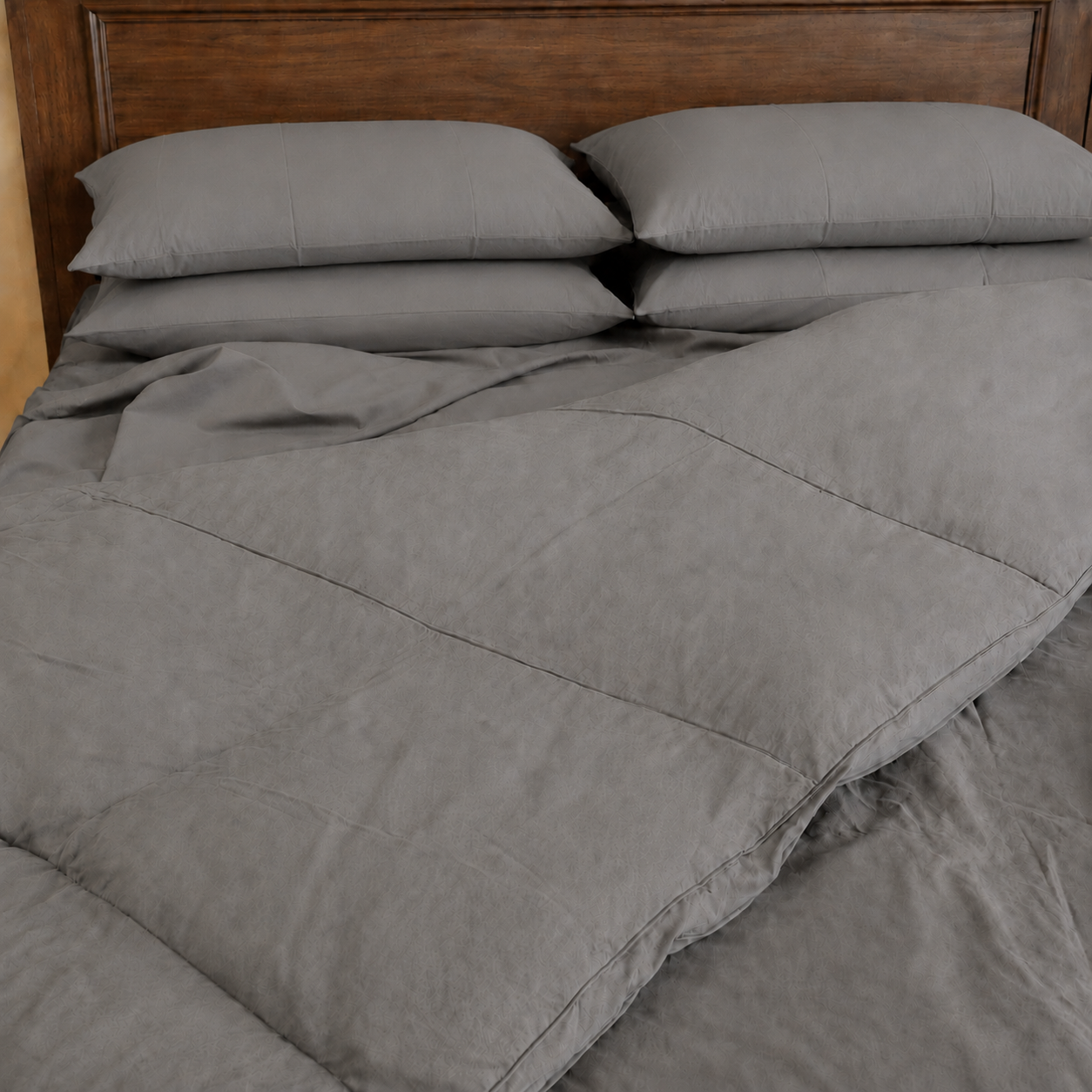 A bed made with a slate sleeping dove cooling comforter and matching pillows, set against a dark brown wooden headboard.