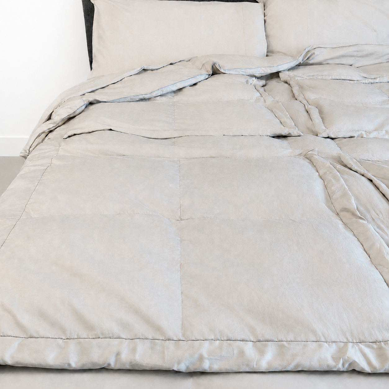Stone sleeping dove cooling comforter or duvet with matching pillowcases on a bed, shown in a clean, minimalist bedroom setting.