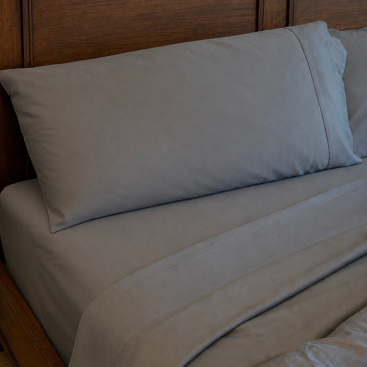Slate sleeping dove bed sheets and a matching pillowcase on a bed with a dark wood headboard.