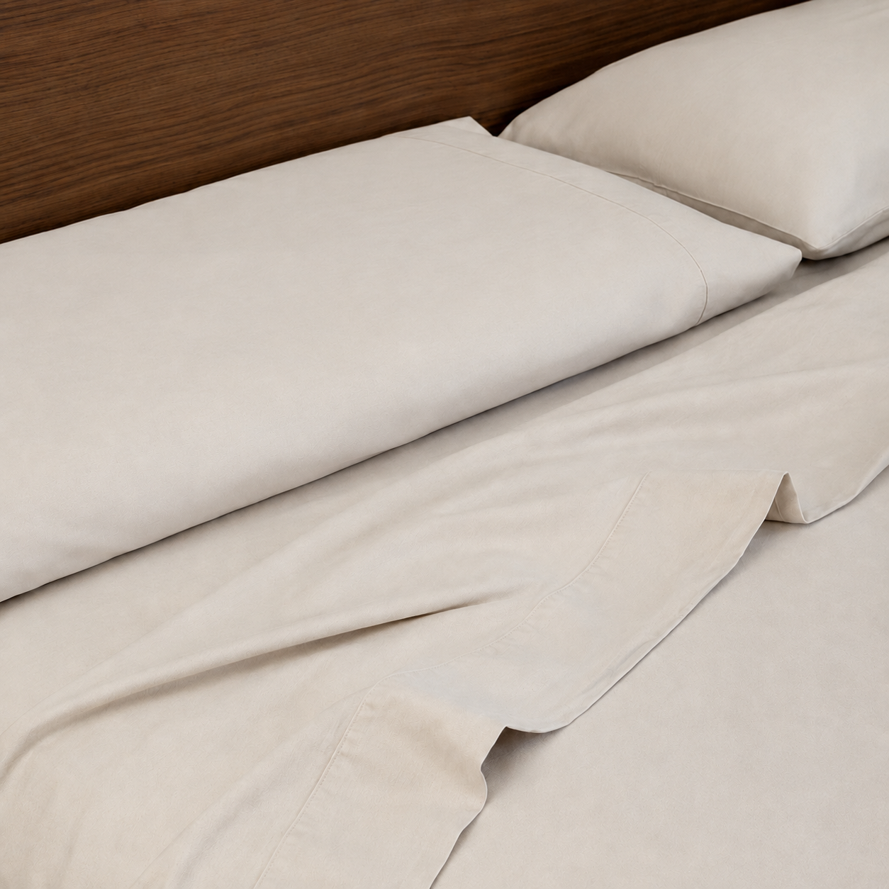 Stone sleeping dove cooling bedding with matching pillowcases and a single corner folded back, shown on a bed with a dark wood headboard.