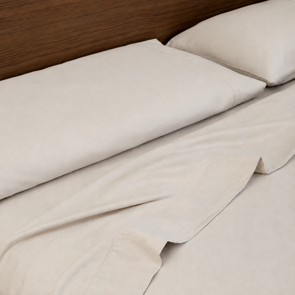 Stone sleeping dove cooling bedding with matching pillowcases and a single corner folded back, shown on a bed with a dark wood headboard.