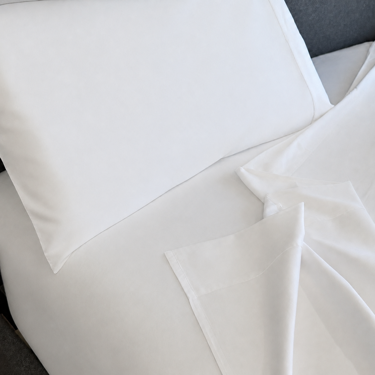 White sleeping dove sheet set with a pillowcase and folded corner of the sheet, shown on a bed.