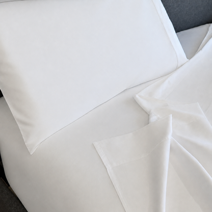 White sleeping dove sheet set with a pillowcase and folded corner of the sheet, shown on a bed.