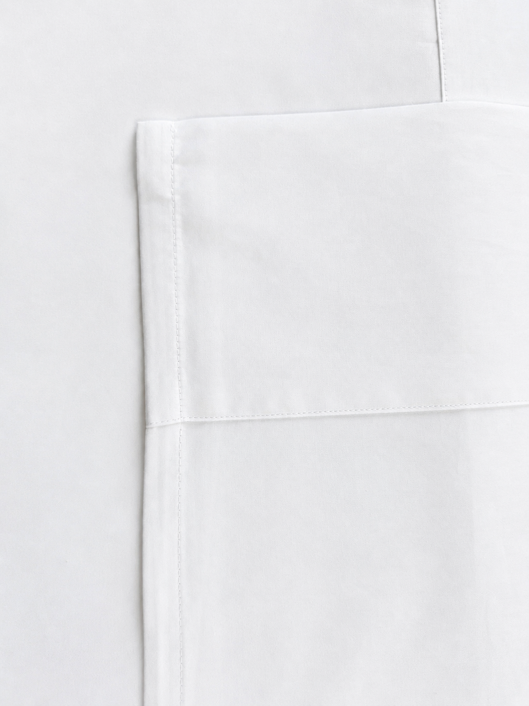 Close-up of a white fabric product showing a folded corner with clean stitching on a matching white background.