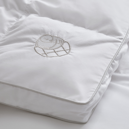 Close-up of the white Sleeping Dove cooling comforter with embroidered logo, made of breathable cotton for hot sleepers, couples, and pet owners. This is the Sleeping Dove Comforter, the natural cooling comforter.